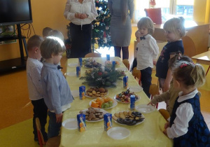 Pani dyrektor Maria Królikowska, pani Anna Tylman oraz dzieci stoją wokół stołu z poczęstunkiem.